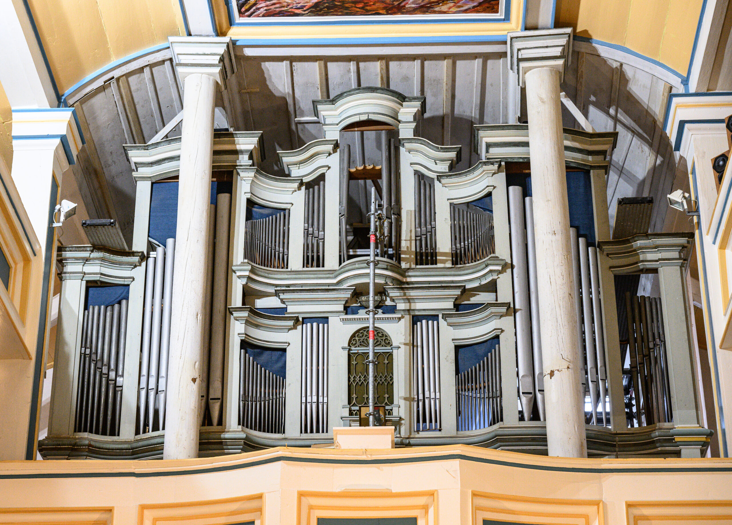 Wölfis
Beeindruckend ist der Blick in das Kirchenschiff der St.-Crucis-Kirche im Ohrdrufer Ortsteil Wölfis, doch es ist noch viel zu tun, im und am sakralen Gebäude im Ortskern vieles so wiederherzustellen, wie es einst mal war. Der Zahn der Zeit nagte reichlich am dem Bauwerk von 1736. 
Noch immer engagiert sich der Gemeindekirchenrat für die Restaurierung der imposanten Ratzmann-Orgel mit ihren 28 zum Teil seltenen Registern, stellt immer wieder Förderanträge und sammelt Spenden. Die Orgel ist ausgebaut und große Teile ihres Inneren liegen in den Werkstätten der Orgelbau Waltershausen GmbH. Dort werden Pfeifen vorintoniert. Die endgültige Intonierung erfolgt nach dem Einbau, unter anderem da sich die Pfeifen dann gegenseitig im Klang beeinflussen können. So erläutert Orgelbaumeister und zugleich einer der beiden Geschäftsführer Joachim Stade den Prozess. 

Die Orgelsanierung inklusive Umfeldarbeiten wird am Ende 222.000 Euro gekostet haben, wird geschätzt. Sie umfasst den auch Umtausch der Pfeifen-Attrappen gegen echte Zinnpfeifen. 
1917 war das Zinn für Kriegszwecke benötigt worden. Umso größer die Freude über einen Besuch des Sparkassen-Chefs für den Kreis Gotha, Jörg Krieglstein und Abteilungsdirektorin Claudia Hemmling. Krieglstein ist zugleich Vorsitzender des Stiftungsvorstandes der Regionalstiftung der Kreissparkasse Gotha. Da auch mithilfe der Vergabe von Pfeifen-Patenschaften Geld einkommen soll, die Ratzmann-Orgel künftig wieder in ganzer Fülle erklingen lassen zu können, übernimmt die Stiftung für 5000 Euro eine dieser Patenschaften. Diese Patenschaften sind zum Teil auch zu deutlich geringeren Spenden zu haben. Wer spendet, kann seinen Namen auf einer der neuen Pfeifen eingravieren lassen. Damit dies auch sichtbar ist, gibt ausserdem den Eintrag auf einer Tafel. Für die Unterstützung in Wölfis haben sich auch Landrat Onno Eckert und Ohrdrufs Bürgermeister Stefan Schambach (beide SPD)  eingesetzt, berichtete Krieglstein. Eckert ist Vorsitzender, Schambach Mitglied des Stiftungsrates. Darüber hinaus soll, diesmal direkt durch die Sparkasse, ein Benefizkonzert mit dem bekannten Gothaer Kirchenmusikdirektor und Organisten Jens Gollhardt unterstützt werden. Erster Orgelpate ist Hans Umbreit, einer der dienstältesten Organisten. Er spielt seit 75 Jahren. Für 1000 Euro übernahm er eine Pfeifen-Patenschaft. 

Viele weitere Reparaturarbeiten stehen für die Kirche an. Die Orgelsanierung betrifft auch deren Umfeld und den Orgel-Prospekt. Nach dem Ausbau der Orgel zeigten sich bröckelnder und mit Hohlräumen durchzogener Putz. Am 19. Februar 2022 implodierte durch Sturm das erste der oberen Turmfenster.  Das Zwillingsfenster daneben war seit den achtziger Jahren abgedeckt, um zu vermeiden, dass die Lederumhüllungen der Blasebälge und der Züge durch die Sonne altern. Hinter der Abdeckung zeigte sich dann ein Schaden an diesem Fenster. Es wäre verantwortungslos gewesen, dies nicht gleich mit zu erneuern, gibt Ursula Rolapp vom Gemeindekirchenrat zu bedenken. Deckleisten über der Orgel wurden mit bereits in der Kirche gelagertem historischem Holz erneuert, damit künftig kein Dreck auf die Orgel rieselt. 

Auch sind Stuckteile an der Decke der ersten Empore zu erneuern. Daran arbeitet zur Zeit eine die Restauratorin Annemarie Grimm aus Arnstadt. In einer Erfurter Werkstatt wird gerade der einzigartige Taufengel der Kirche durch Heike Glaß restauriert. 

St. Crucis hat Erkerfenster. Die Erker wurden 1983 entfernt, um das Dach einfacher abzudichten. Die Kirche sei daraufhin innen sehr dunkel gewesen, erinnert sich Gunar Rolapp, ein Gemeindemitglied, das auch selbst viele Arbeiten in der Kirche übernimmt. In den neunziger Jahren wurden die Erker wieder neu gebaut, um den ursprünglichen Zustand wieder herzustellen. Doch inzwischen haben zwei davon Schäden, wie sich beim ersten neuen Anstrich seit den neunziger Jahren zeigte.

In die Höhe muss auch noch ein inzwischen neu fertiggestelltes zweites Zifferblatt der Turmuhr. Das alte Zifferblatt war ebenfalls durch den Sturm beschädigt. 

So kommen in jedem Bauabschnitt - allein für die Orgel sind es vier - unerwartete Kosten hinzu, berichtet Ursula Rolapp. Deshalb sammelt der Gemeindekirchenrat weiterhin Spenden. Wer helfen möchte, kann unter dem Verwendungszweck „Ratzmann-Orgel Wölfis“ an die Evangelische Kirchgemeinde Wölfis auf IBAN DE 28 8206 4038 0000 2906 10  (VR Bank Westthüringen) spenden. Wer Spendenquittung möchte, sollte bitte zusätzlich zum Verwendungszweck Name und Wohnanschrift vermerken. 

Unter dem Verwendungszweck „Engel“ ist unter der selben Bankverbindung auch eine Unterstützung der Restaurierung des Taufengels der Kirche möglich. Wer Pate einer Orgelpfeife werden möchte, gibt als Verwendungszweck (Kennwort) „Pfeifenpatenschaft“ an. Die Beträge in Euro richten sich danach, auf welcher Pfeife die Inschrift mit dem Namen des Spenders eingraviert und damit für die Nachwelt erhalten bleiben soll. 