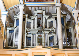 Wölfis Beeindruckend ist der Blick in das Kirchenschiff der St.-Crucis-Kirche im Ohrdrufer Ortsteil Wölfis, doch es ist noch viel zu tun, im und am sakralen Gebäude im Ortskern vieles so wiederherzustellen, wie es einst mal war. Der Zahn der Zeit nagte reichlich am dem Bauwerk von 1736. Noch immer engagiert sich der Gemeindekirchenrat für die Restaurierung der imposanten Ratzmann-Orgel mit ihren 28 zum Teil seltenen Registern, stellt immer wieder Förderanträge und sammelt Spenden. Die Orgel ist ausgebaut und große Teile ihres Inneren liegen in den Werkstätten der Orgelbau Waltershausen GmbH. Dort werden Pfeifen vorintoniert. Die endgültige Intonierung erfolgt nach dem Einbau, unter anderem da sich die Pfeifen dann gegenseitig im Klang beeinflussen können. So erläutert Orgelbaumeister und zugleich einer der beiden Geschäftsführer Joachim Stade den Prozess. Die Orgelsanierung inklusive Umfeldarbeiten wird am Ende 222.000 Euro gekostet haben, wird geschätzt. Sie umfasst den auch Umtausch der Pfeifen-Attrappen gegen echte Zinnpfeifen. 1917 war das Zinn für Kriegszwecke benötigt worden. Umso größer die Freude über einen Besuch des Sparkassen-Chefs für den Kreis Gotha, Jörg Krieglstein und Abteilungsdirektorin Claudia Hemmling. Krieglstein ist zugleich Vorsitzender des Stiftungsvorstandes der Regionalstiftung der Kreissparkasse Gotha. Da auch mithilfe der Vergabe von Pfeifen-Patenschaften Geld einkommen soll, die Ratzmann-Orgel künftig wieder in ganzer Fülle erklingen lassen zu können, übernimmt die Stiftung für 5000 Euro eine dieser Patenschaften. Diese Patenschaften sind zum Teil auch zu deutlich geringeren Spenden zu haben. Wer spendet, kann seinen Namen auf einer der neuen Pfeifen eingravieren lassen. Damit dies auch sichtbar ist, gibt ausserdem den Eintrag auf einer Tafel. Für die Unterstützung in Wölfis haben sich auch Landrat Onno Eckert und Ohrdrufs Bürgermeister Stefan Schambach (beide SPD) eingesetzt, berichtete Krieglstein. Eckert ist Vorsitzender, Schambach Mitglied des Stiftungsrates. Darüber hinaus soll, diesmal direkt durch die Sparkasse, ein Benefizkonzert mit dem bekannten Gothaer Kirchenmusikdirektor und Organisten Jens Gollhardt unterstützt werden. Erster Orgelpate ist Hans Umbreit, einer der dienstältesten Organisten. Er spielt seit 75 Jahren. Für 1000 Euro übernahm er eine Pfeifen-Patenschaft. Viele weitere Reparaturarbeiten stehen für die Kirche an. Die Orgelsanierung betrifft auch deren Umfeld und den Orgel-Prospekt. Nach dem Ausbau der Orgel zeigten sich bröckelnder und mit Hohlräumen durchzogener Putz. Am 19. Februar 2022 implodierte durch Sturm das erste der oberen Turmfenster. Das Zwillingsfenster daneben war seit den achtziger Jahren abgedeckt, um zu vermeiden, dass die Lederumhüllungen der Blasebälge und der Züge durch die Sonne altern. Hinter der Abdeckung zeigte sich dann ein Schaden an diesem Fenster. Es wäre verantwortungslos gewesen, dies nicht gleich mit zu erneuern, gibt Ursula Rolapp vom Gemeindekirchenrat zu bedenken. Deckleisten über der Orgel wurden mit bereits in der Kirche gelagertem historischem Holz erneuert, damit künftig kein Dreck auf die Orgel rieselt. Auch sind Stuckteile an der Decke der ersten Empore zu erneuern. Daran arbeitet zur Zeit eine die Restauratorin Annemarie Grimm aus Arnstadt. In einer Erfurter Werkstatt wird gerade der einzigartige Taufengel der Kirche durch Heike Glaß restauriert. St. Crucis hat Erkerfenster. Die Erker wurden 1983 entfernt, um das Dach einfacher abzudichten. Die Kirche sei daraufhin innen sehr dunkel gewesen, erinnert sich Gunar Rolapp, ein Gemeindemitglied, das auch selbst viele Arbeiten in der Kirche übernimmt. In den neunziger Jahren wurden die Erker wieder neu gebaut, um den ursprünglichen Zustand wieder herzustellen. Doch inzwischen haben zwei davon Schäden, wie sich beim ersten neuen Anstrich seit den neunziger Jahren zeigte. In die Höhe muss auch noch ein inzwischen neu fertiggestelltes zweites Zifferblatt der Turmuhr. Das alte Zifferblatt war ebenfalls durch den Sturm beschädigt. So kommen in jedem Bauabschnitt - allein für die Orgel sind es vier - unerwartete Kosten hinzu, berichtet Ursula Rolapp. Deshalb sammelt der Gemeindekirchenrat weiterhin Spenden. Wer helfen möchte, kann unter dem Verwendungszweck „Ratzmann-Orgel Wölfis“ an die Evangelische Kirchgemeinde Wölfis auf IBAN DE 28 8206 4038 0000 2906 10 (VR Bank Westthüringen) spenden. Wer Spendenquittung möchte, sollte bitte zusätzlich zum Verwendungszweck Name und Wohnanschrift vermerken. Unter dem Verwendungszweck „Engel“ ist unter der selben Bankverbindung auch eine Unterstützung der Restaurierung des Taufengels der Kirche möglich. Wer Pate einer Orgelpfeife werden möchte, gibt als Verwendungszweck (Kennwort) „Pfeifenpatenschaft“ an. Die Beträge in Euro richten sich danach, auf welcher Pfeife die Inschrift mit dem Namen des Spenders eingraviert und damit für die Nachwelt erhalten bleiben soll.